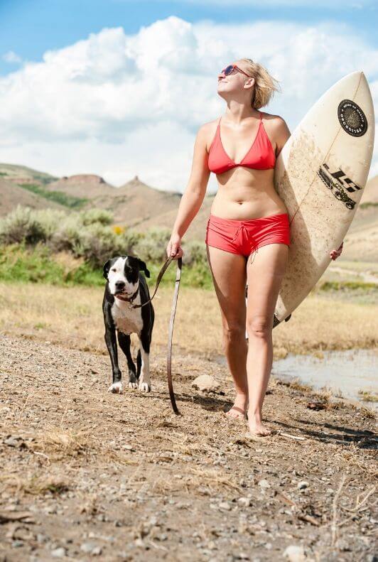 Surfista con bikini rosso e pantaloncini che passeggia col cane in spiaggia